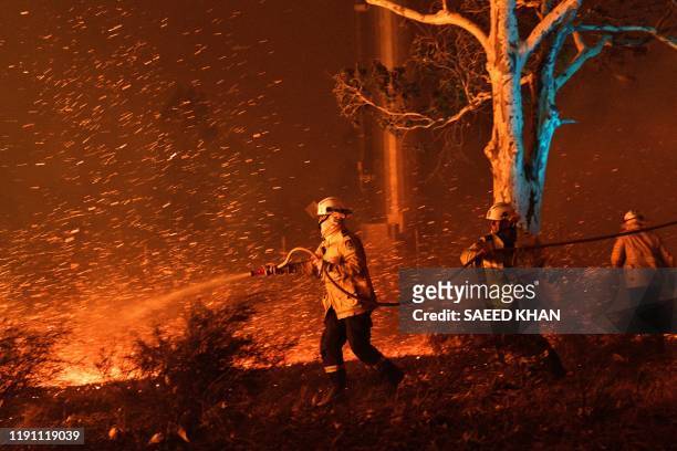 This picture taken on December 31, 2019 shows firefighters hosing down embers to secure nearby houses from bushfires near the town of Nowra in the...