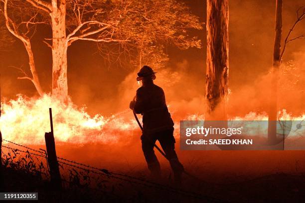 This picture taken on December 31, 2019 shows a firefighter hosing down trees and flying embers in an effort to secure nearby houses from bushfires...