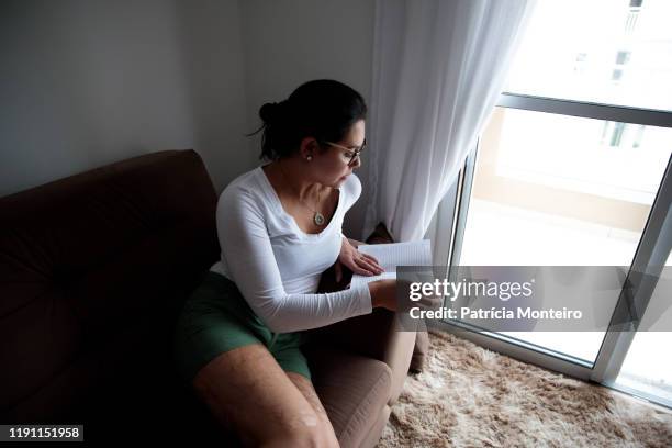 mulher lendo livro e estudando, na sala de sua casa - lendo fotografías e imágenes de stock