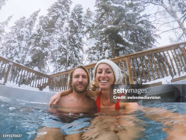 young couple taking selfie in spa hot tub in winter surrounded by snow young couple taking selfie in spa hot tub in winter surrounded by snow - hot tub stock pictures, royalty-free photos & images