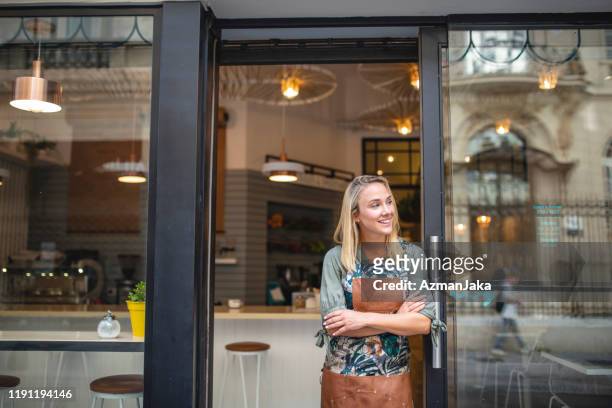 giovane proprietario del caffè in piedi con le braccia incrociate alla porta d'ingresso - attività del fine settimana foto e immagini stock