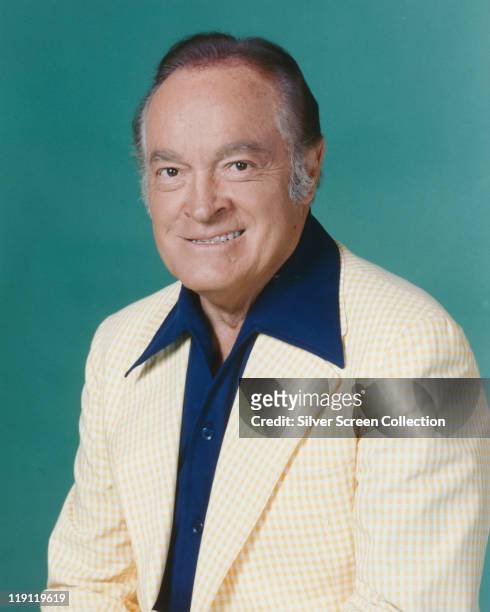 Bob Hope , British actor and comedian, wearing a white jacket and dark blue shirt in a studio portrait, against a petrol blue background, circa 1960.
