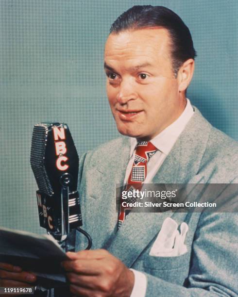 Bob Hope , British actor and comedian, posing beside an NBC microphone in a studio portrait, against a light blue background, circa 1950.