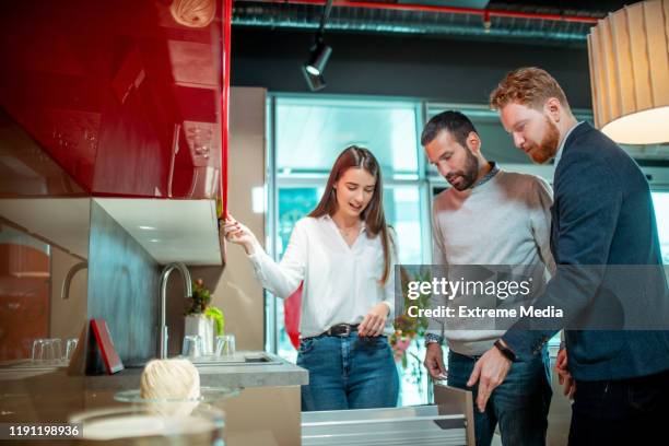 a store clerk demonstrating some kitchen design ideas and opening a cabinet drawer for a young couple in a kitchen equipment store - kitchen clerk stock pictures, royalty-free photos & images