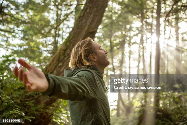 jonge man omarmen regenwoud staande in zonnestralen verlichten van de bomen - inhaling stockfoto's en -beelden