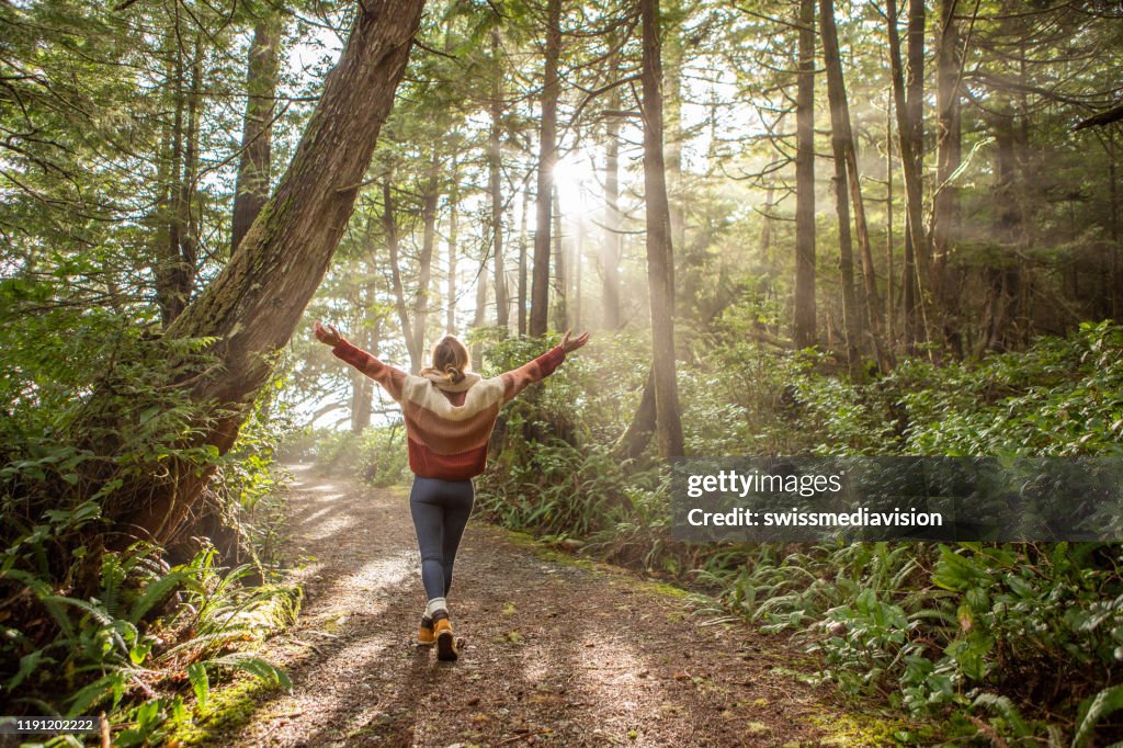 Young woman embracing rainforest standing in sunbeams illuminating the trees