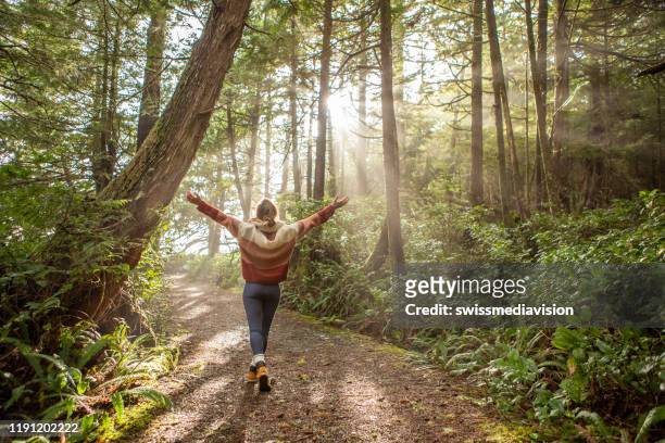 young woman embracing rainforest standing in sunbeams illuminating the trees - recovery stock pictures, royalty-free photos & images