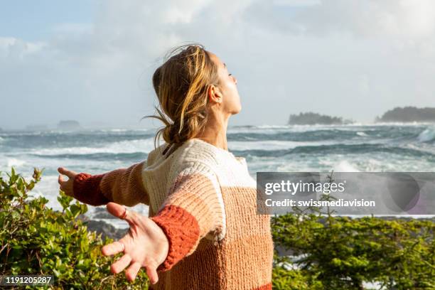 young woman standing on coastline arms outstretched, wilderness area - canadian pacific women stock pictures, royalty-free photos & images