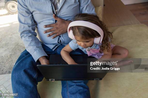 Father trying to use on a laptop at home while young child tries to press the keyboard