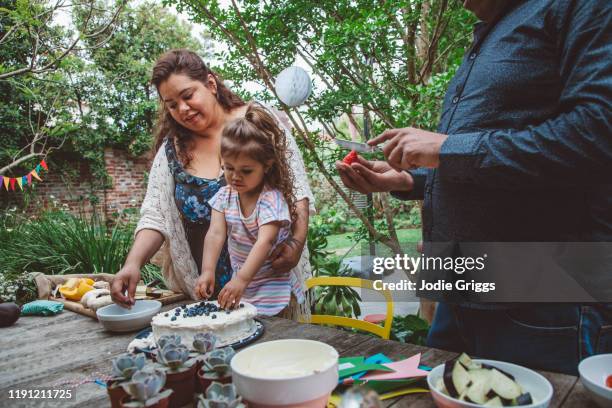 Family decorating a cake together during a celebration in the backyard