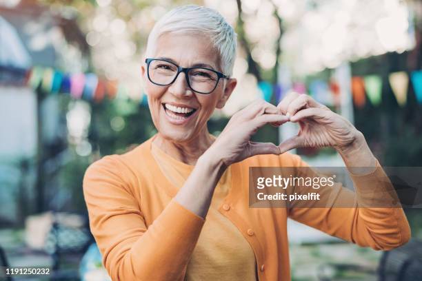 lovely mature woman making heart shape with hands - woman signing stock pictures, royalty-free photos & images