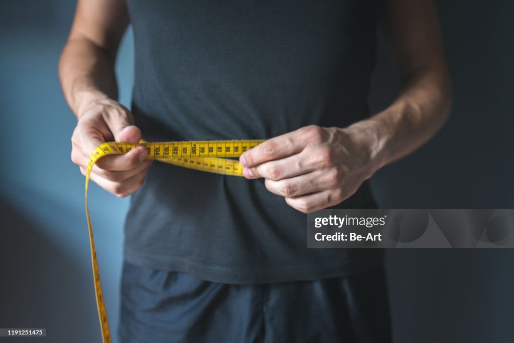 Slim man measuring his waist. Healthy lifestyle, body slimming, weight loss concept.