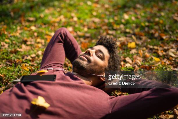 relaxed young man laying on ground and listening to music on autumn day. - laying park stock pictures, royalty-free photos & images