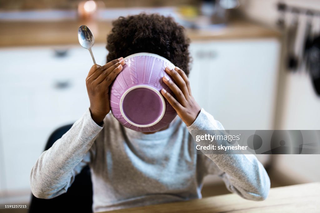 Small black kid eating his breakfast from a bowl at dining table.