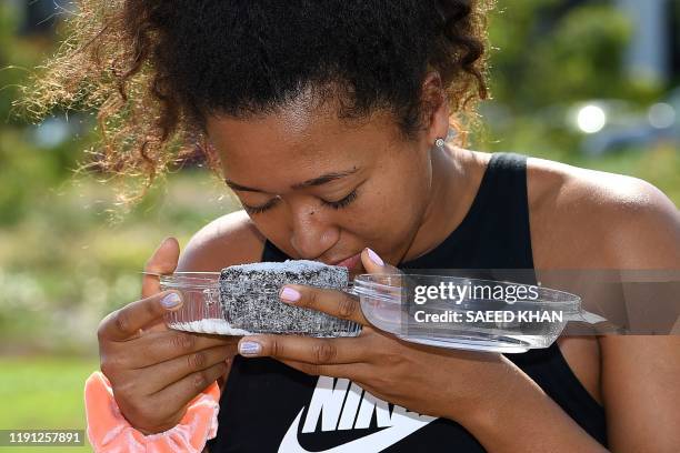 Tennis player Naomi Osaka of Japan tries a lamington cake after taking a sightseeing ride in a helicopter at the Queensland Tennis Centre in Brisbane...