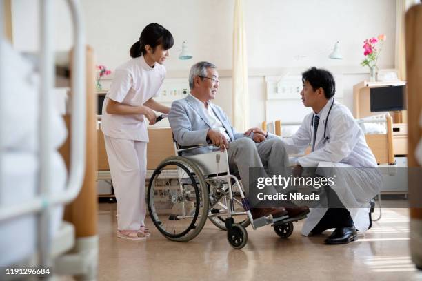 male doctor discussing with senior man sitting on wheelchair in hospital ward - japan and medical and hospital stock pictures, royalty-free photos & images