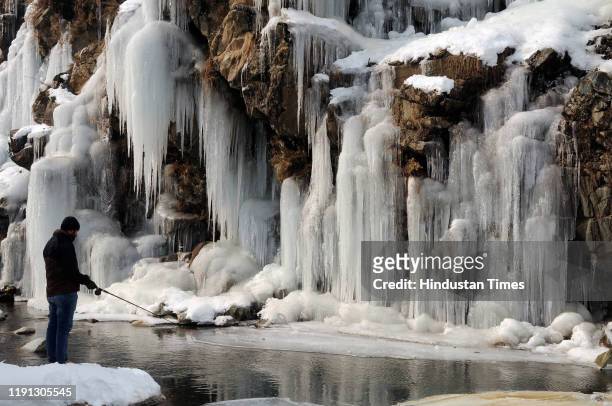 Man fishes near a frozen waterfall in the Drang area of Tangmarg, north of Srinagar, on January 2, 2020 in Srinagar, India.