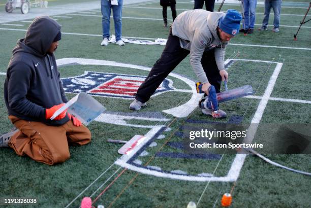 Workers spray paint the NFL Wild Card logo onto the field during press conferences in advance of the AFC Wild Card Game between the New England...