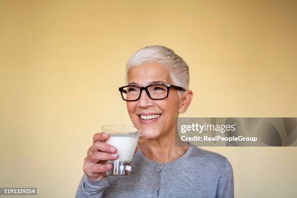 cheerful mature woman enjoying in glass of milk at home. - woman drinking milk stock pictures, royalty-free photos & images