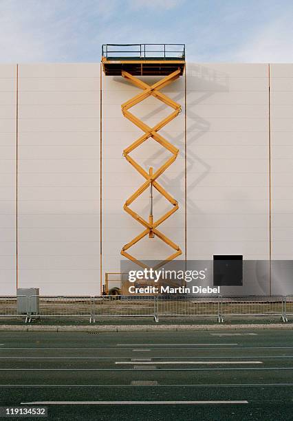 a hydraulic platform raised next to a building - construction barrier stock-fotos und bilder