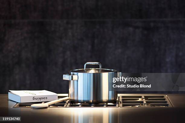 saucepan, cookery book and wooden spoon on hob. - kochgeschirr stock-fotos und bilder