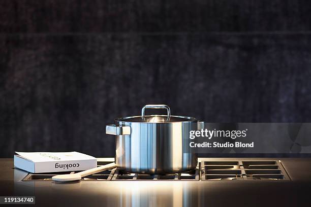saucepan, cookery book and wooden spoon on hob. - pot foto e immagini stock