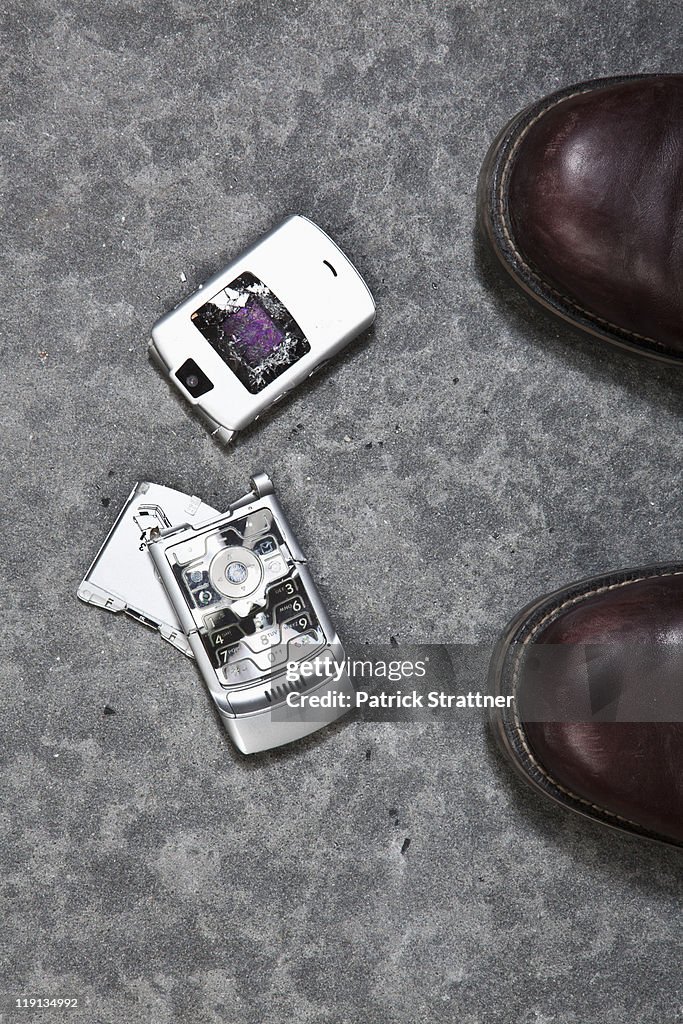 Two booted feet next to a smashed mobile phone