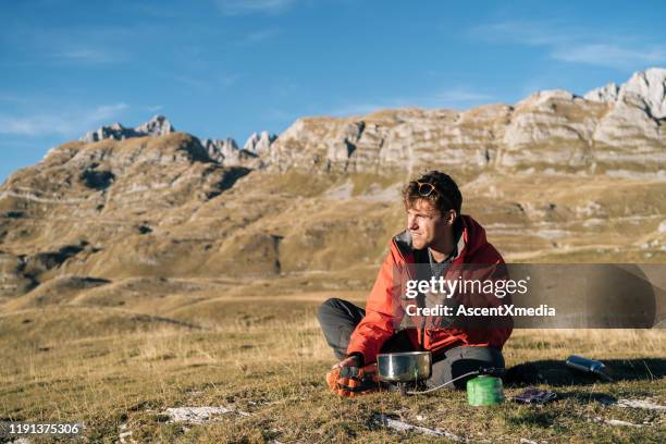 backpacker prepares meal on camp stove in mountains - survival food stock pictures, royalty-free photos & images