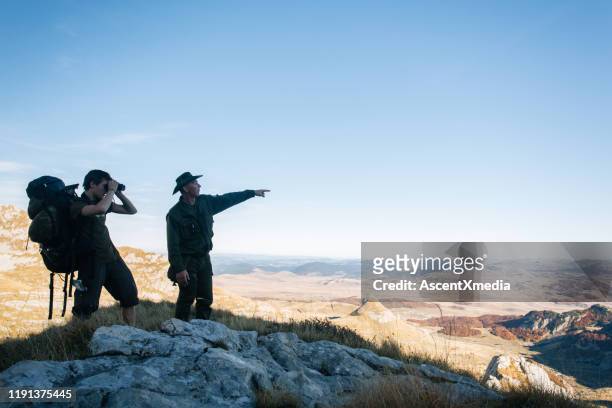 o homem novo e o guia usam binóculos nas montanhas - guide - fotografias e filmes do acervo
