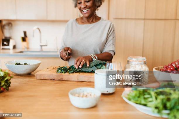 senior vrouwelijke hakken groente op keukeneiland - black cook stockfoto's en -beelden
