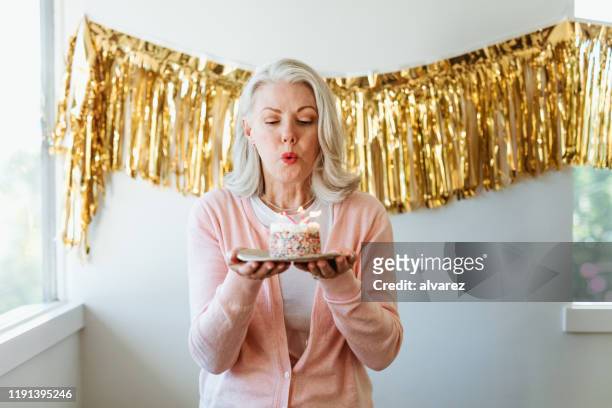 woman blowing burning candles on birthday cake - senior woman birthday stock pictures, royalty-free photos & images