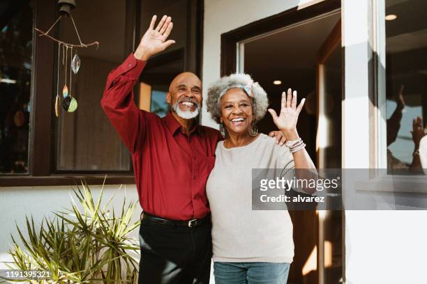 pensionato sorridente in piedi con il braccio intorno alla moglie - sventolare la mano foto e immagini stock