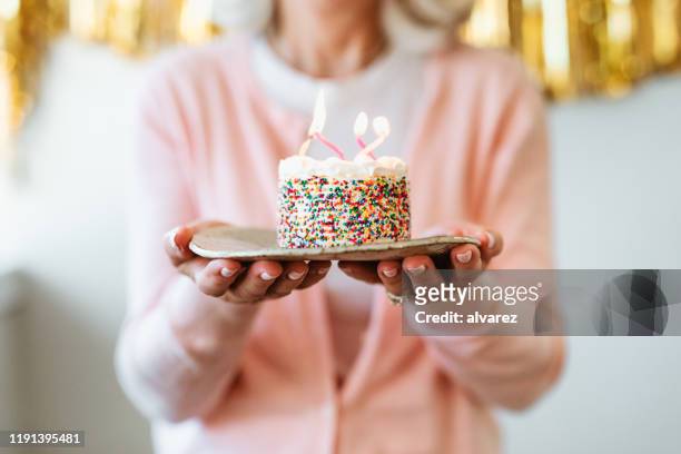 gepensioneerde vrouw met cake met verjaardag kaarsen - birthday stockfoto's en -beelden
