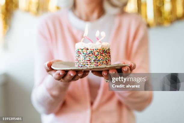 retired woman holding cake with birthday candles - birthday cake imagens e fotografias de stock