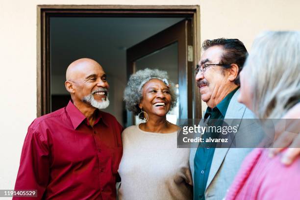 smiling retired senior friends talking at doorway - los angeles garden party stock pictures, royalty-free photos & images