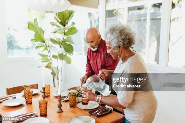 mujer mayor vertiendo agua en vidrio por marido - chorro agua fotografías e imágenes de stock