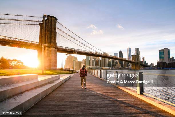 one man walking on the old dock under brooklyn bridge at sunset, new york city - hudson river stock pictures, royalty-free photos & images