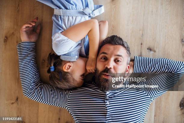 top view of mature father and small daughter lying on floor indoors at home, whispering. - chuchoter photos et images de collection