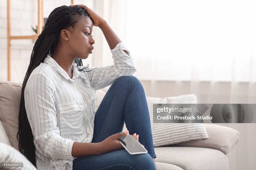 Upset Afro Girl Sitting On Couch With Cellphone, Thinking About Something