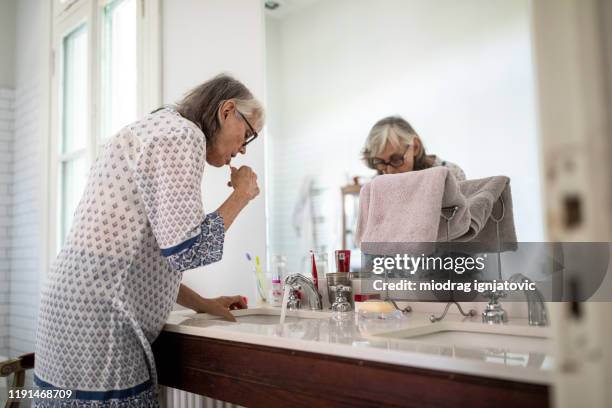 senior woman brushing her teeth in bathroom - bathroom senior stock pictures, royalty-free photos & images