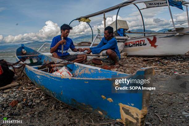 Two fishermen working on a torn fishing net. High waves in the waters of Palu Bay forced Hundreds of fishermen in the village of Lere to anchor their...