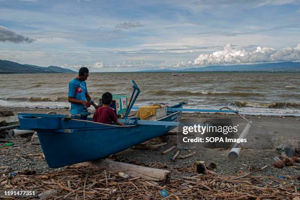 Fisherman accompanied by his son repairing a broken boat engine. High waves in the waters of Palu Bay forced Hundreds of fishermen in the village of...