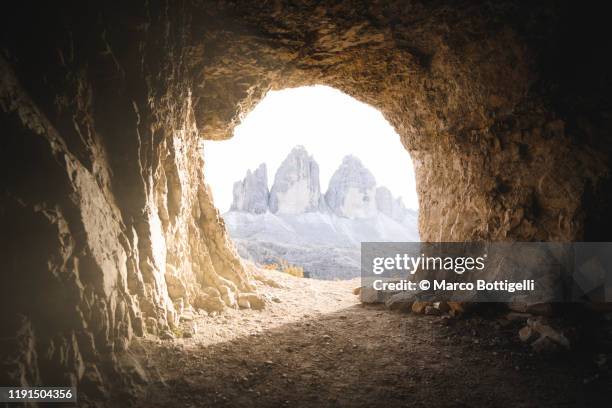 three peaks of lavaredo seen through a cavern entrance, italy - höhle stock-fotos und bilder