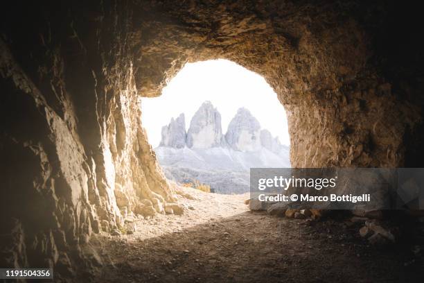 three peaks of lavaredo seen through a cavern entrance, italy - grotta foto e immagini stock