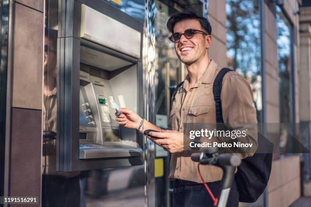 man withdrawing money at the atm - man atm smile stock pictures, royalty-free photos & images