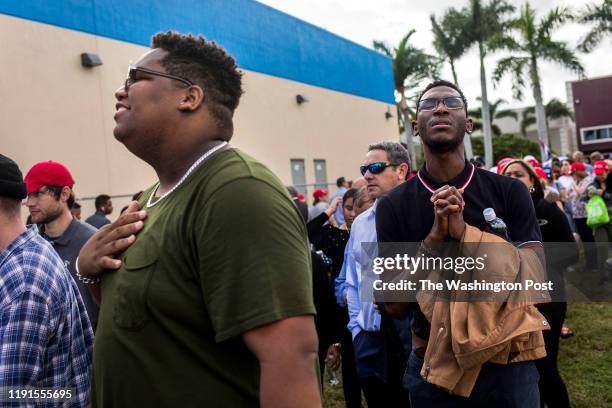 Heath King, left, and Kamarick Mackey, right, sing along with the Christian music being played over the loud speakers while waiting in line at the...