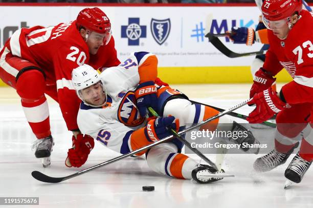 Cal Clutterbuck of the New York Islanders falls to the ice trying to get around the sticks of Dylan McIlrath and Adam Erne of the Detroit Red Wings...