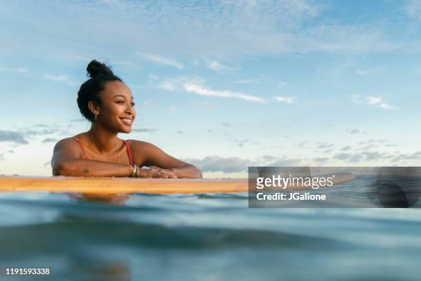 young woman resting on her surfboard waiting for a wave - african woman swimming stock pictures, royalty-free photos & images