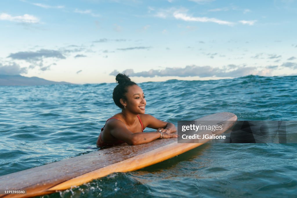 Junge Frau ruht sich auf ihrem Surfbrett und wartet auf eine Welle