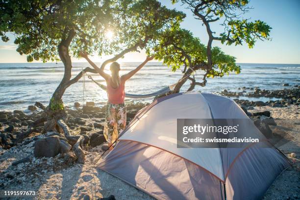 joven acampando en la playa se encuentra los brazos de par en par frente a la tienda de campaña al atardecer - big island hawaii islands fotografías e imágenes de stock